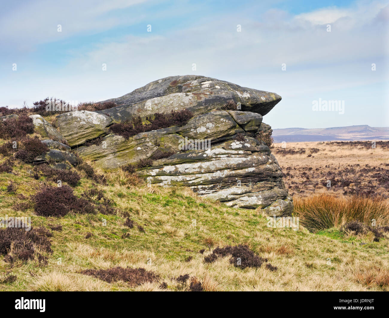 Gritstone rock formation partialy covered by grass and dry brown Stock