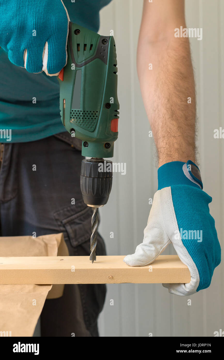 Carpenter handyman using electric drill to make holes on plank on the woodwork workshop table Stock Photo