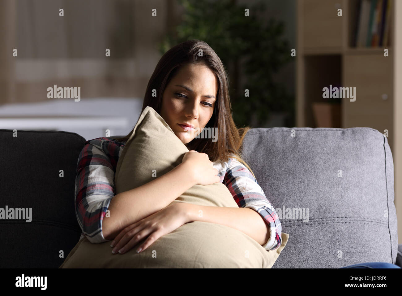 Front view of a sad single girl embracing a pillow sitting on a couch ...