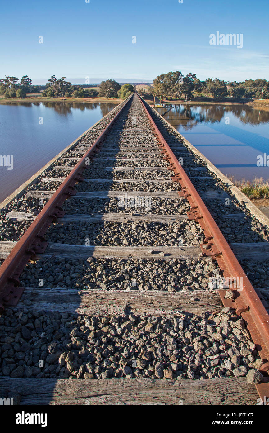 Railway Lines to the Horizon at the Disused Railway Bridge over Joyces Creek at its entry to Lake Cairn Curran. Newstead, Victoria, Australia Stock Photo