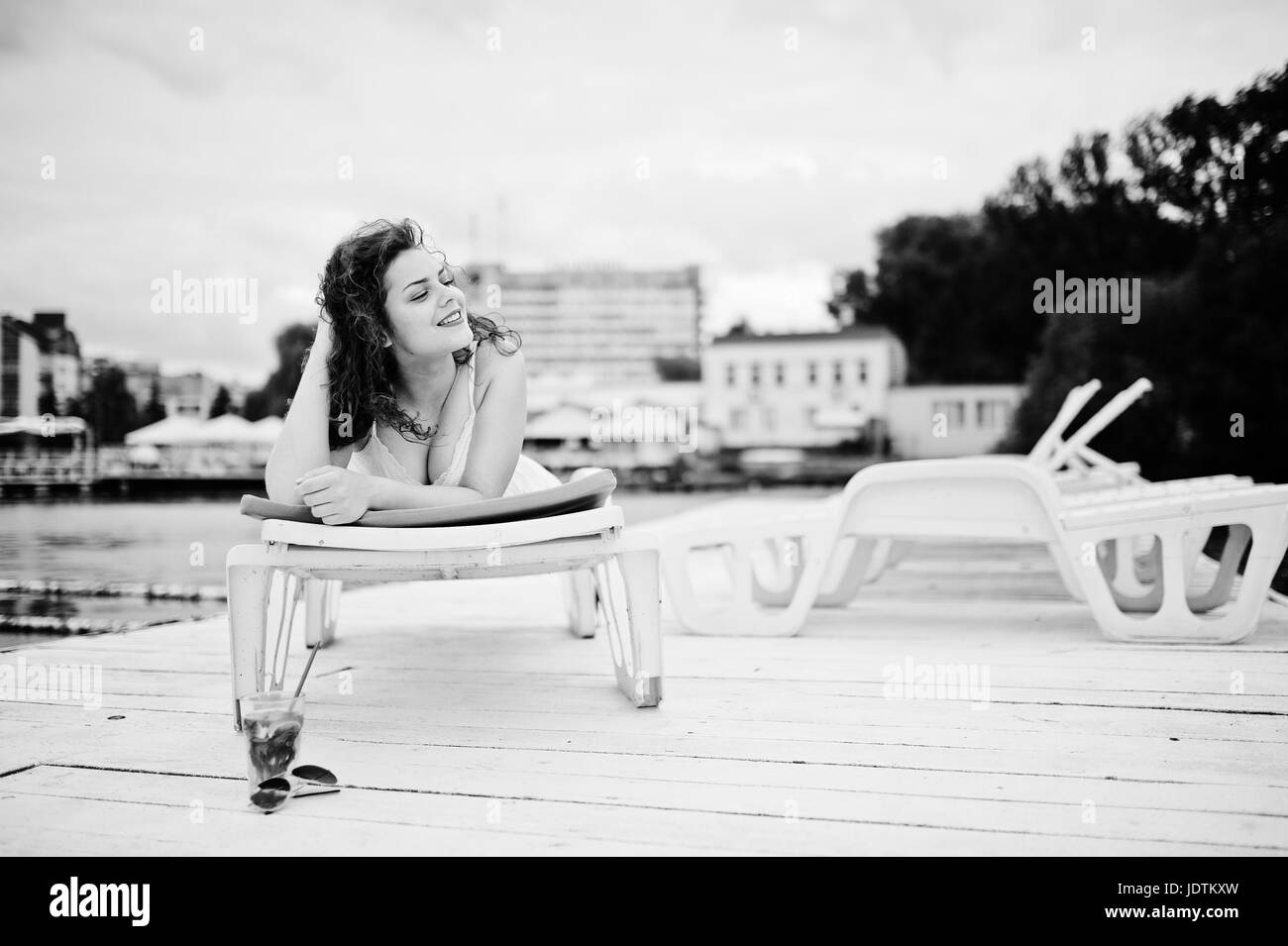 Portrait of a very beautiful girl laying and posing on a launger on a lakeside. Black and white photo. Stock Photo