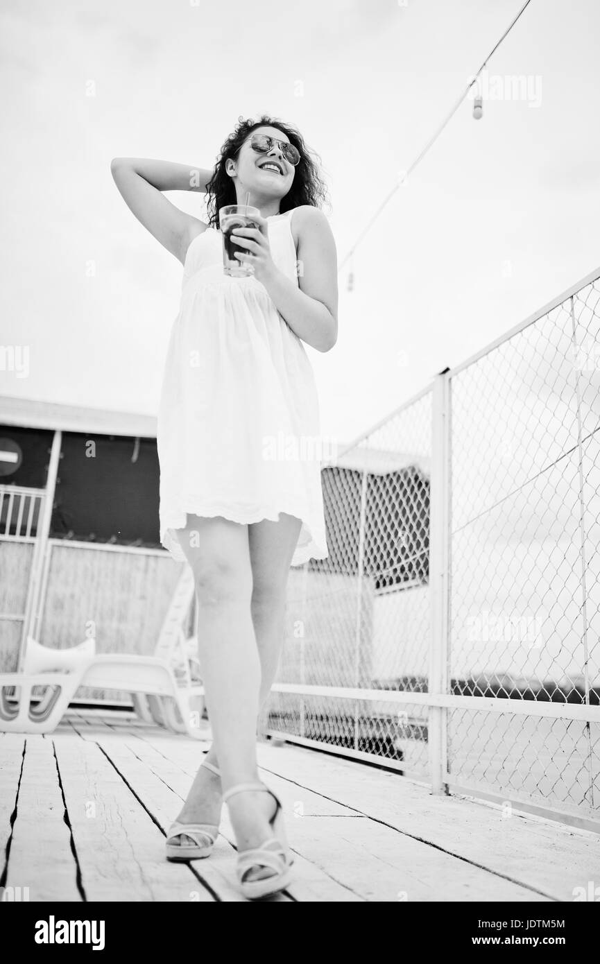 Portrait of an attractive young woman posing with her cocktail on a lakeside wearing sunglasses. Black and white photo. Stock Photo