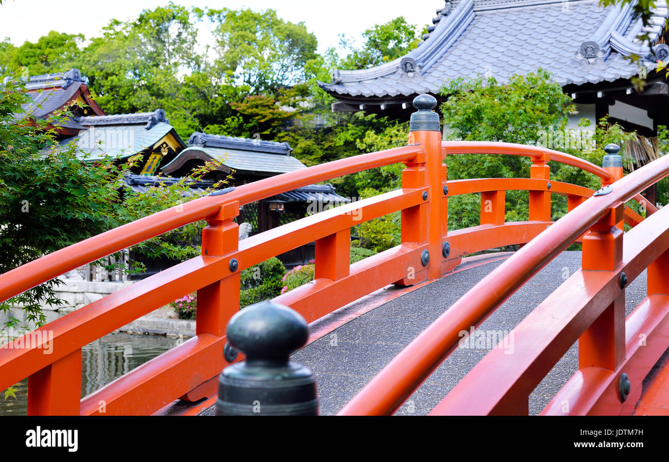 A vermilion arched footbridge going over a pond with Shinsen'en Shrine in the background, Kyoto, Japan Stock Photo