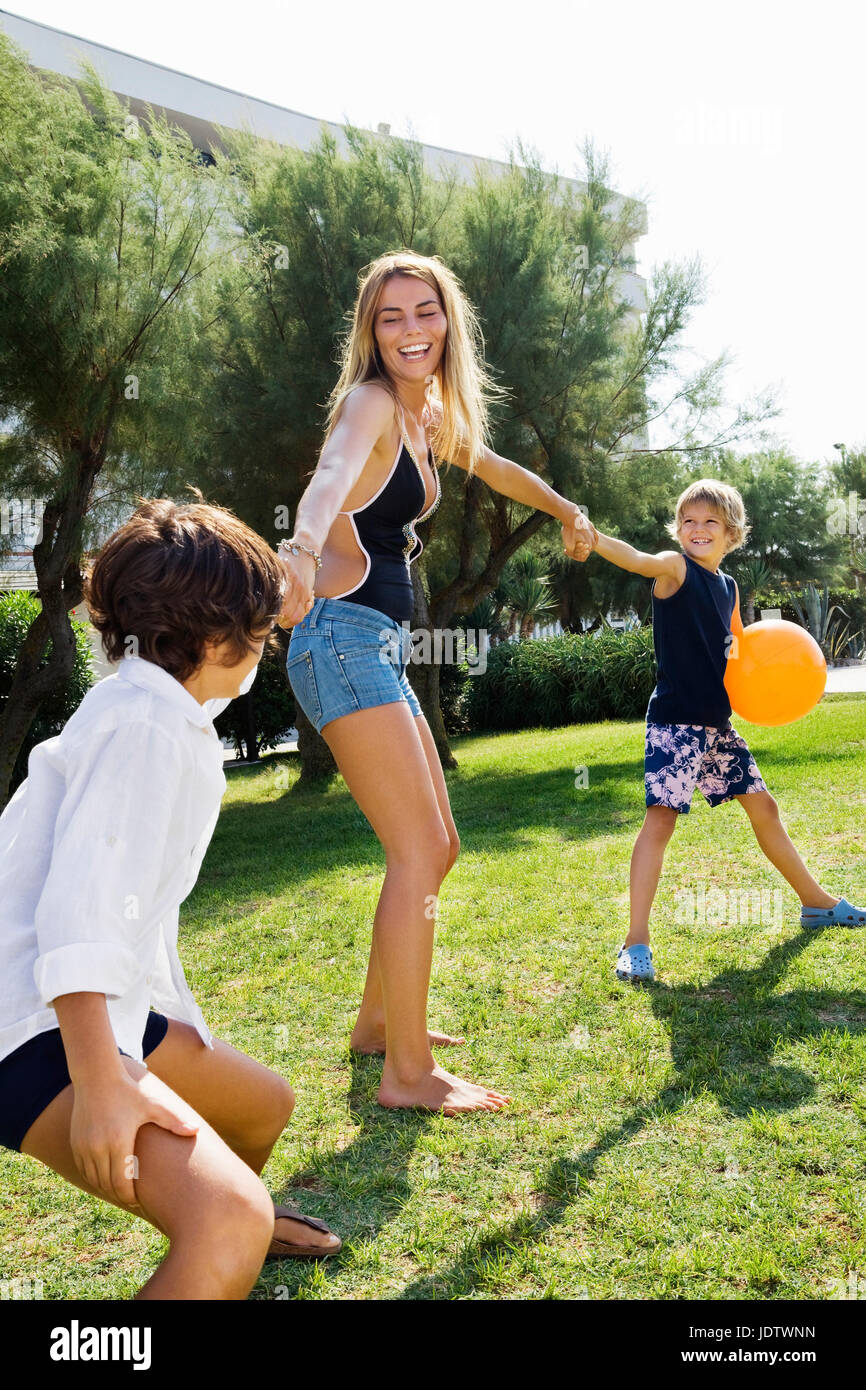 Kids pulling young woman's hand on lawn Stock Photo