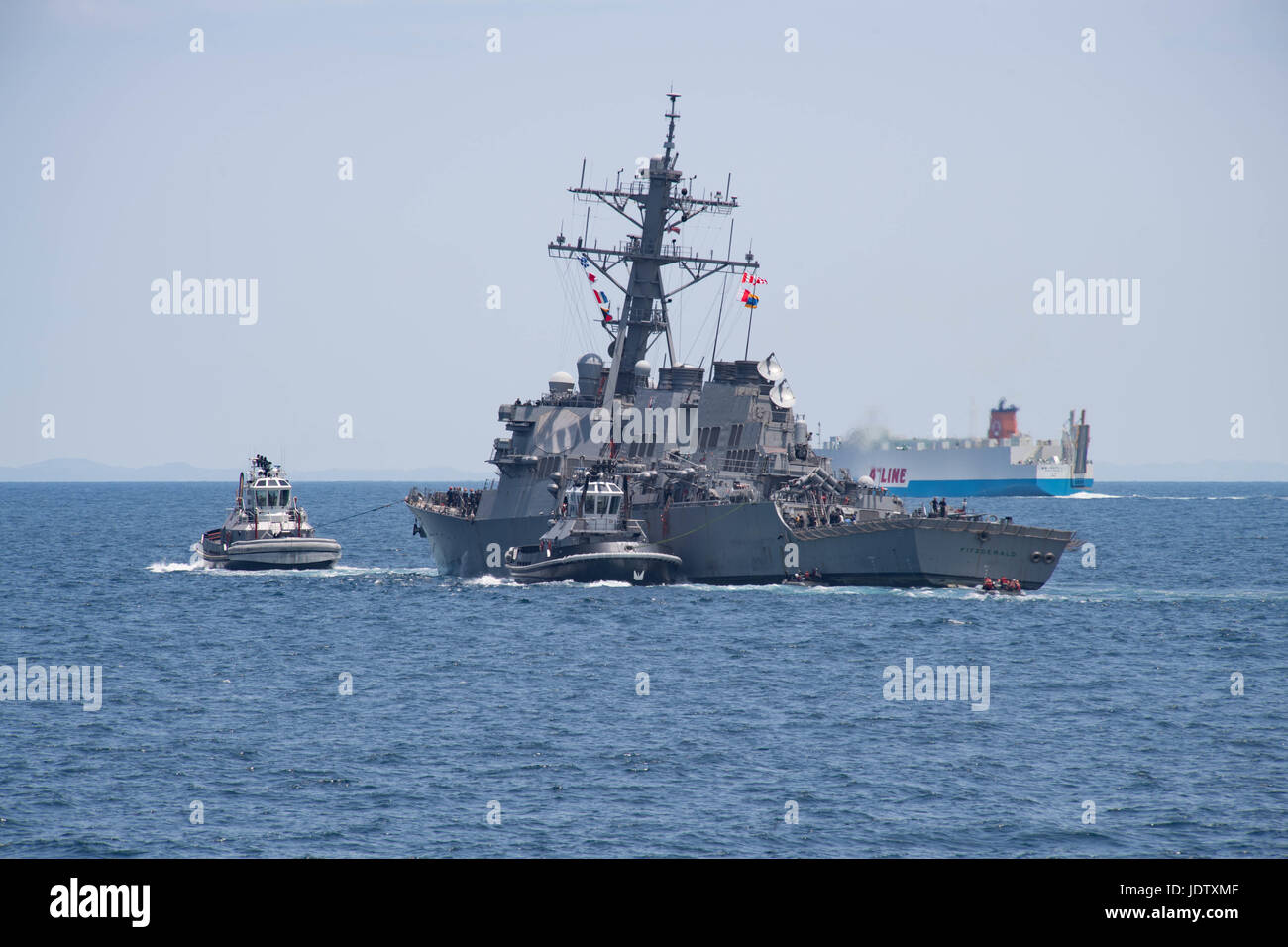 U.S Navy Arleigh Burke-class guided missile destroyer USS Fitzgerald is assisted by tug boats as it returns to port following a collision at sea with a merchant vessel June 17, 2017 in  Yokosuka, Japan. The collision resulted in the death of seven sailors and extensive damage to the warship. Stock Photo