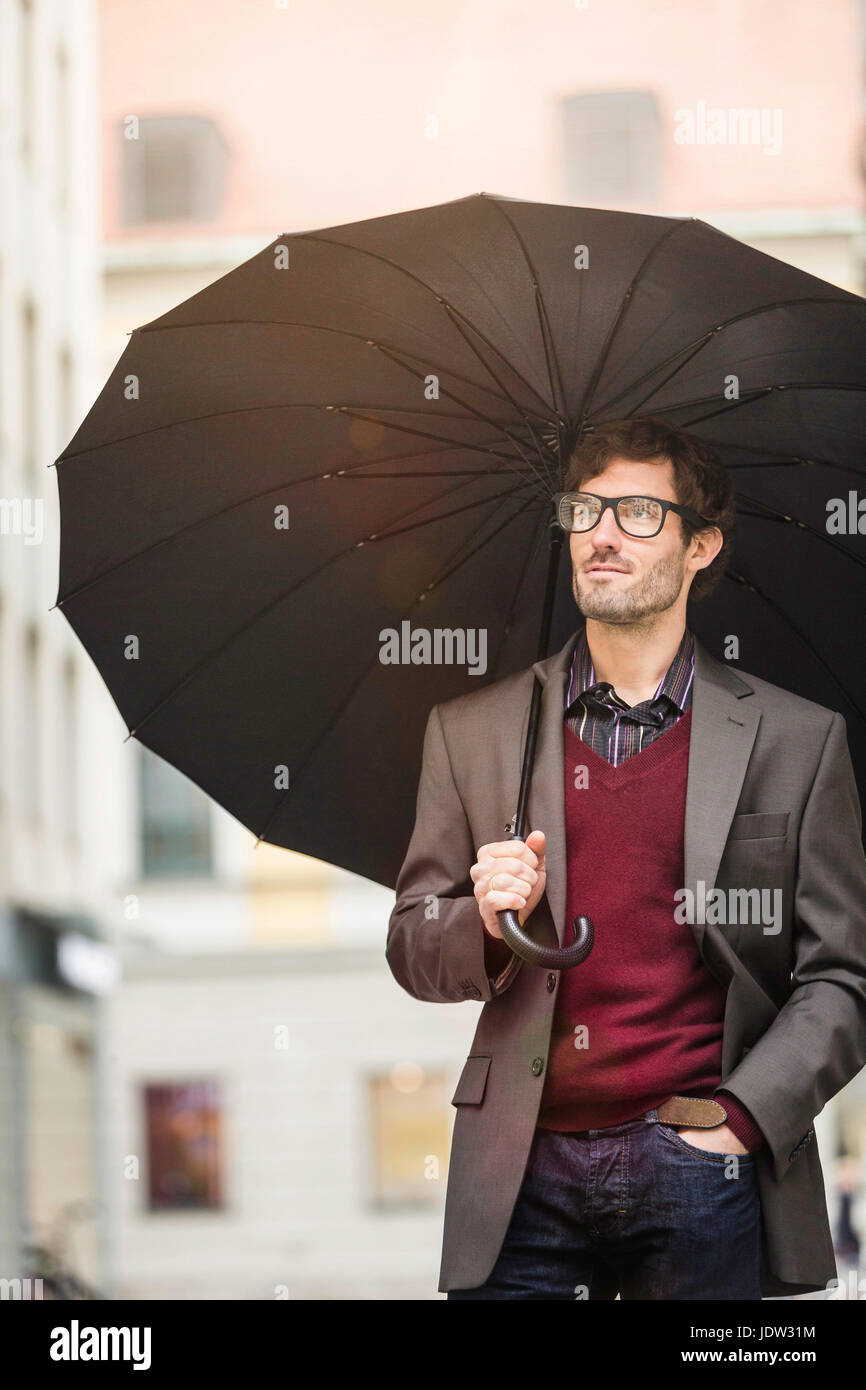 Man carrying umbrella on city street Stock Photo