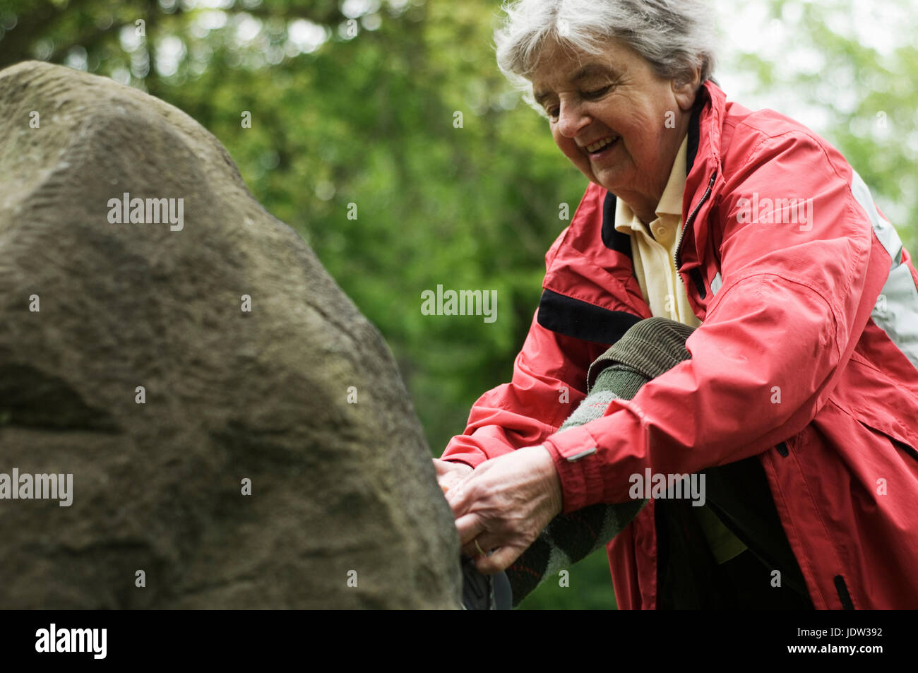 Older woman tying shoe on rock in park Stock Photo