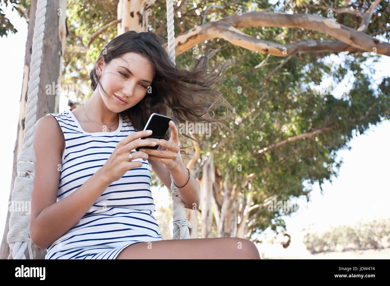 Young adult woman sitting on swing using smartphone Stock Photo