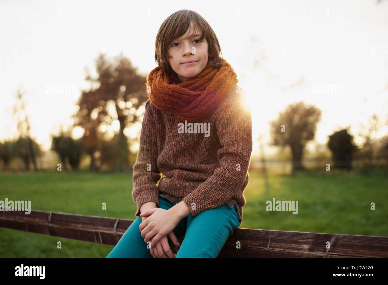 Boy in scarf sitting on fence in countryside, portrait Stock Photo
