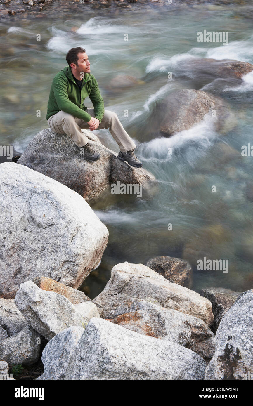 Mid adult man sitting on rocks in river Stock Photo