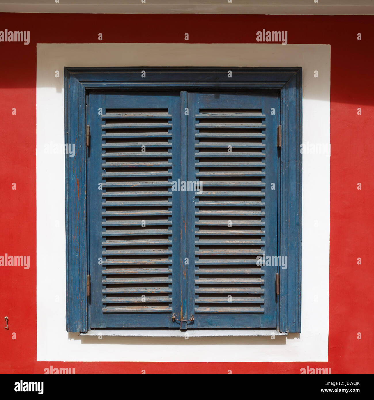 A beautiful old window on a red wall with closed blue shutters. The ...
