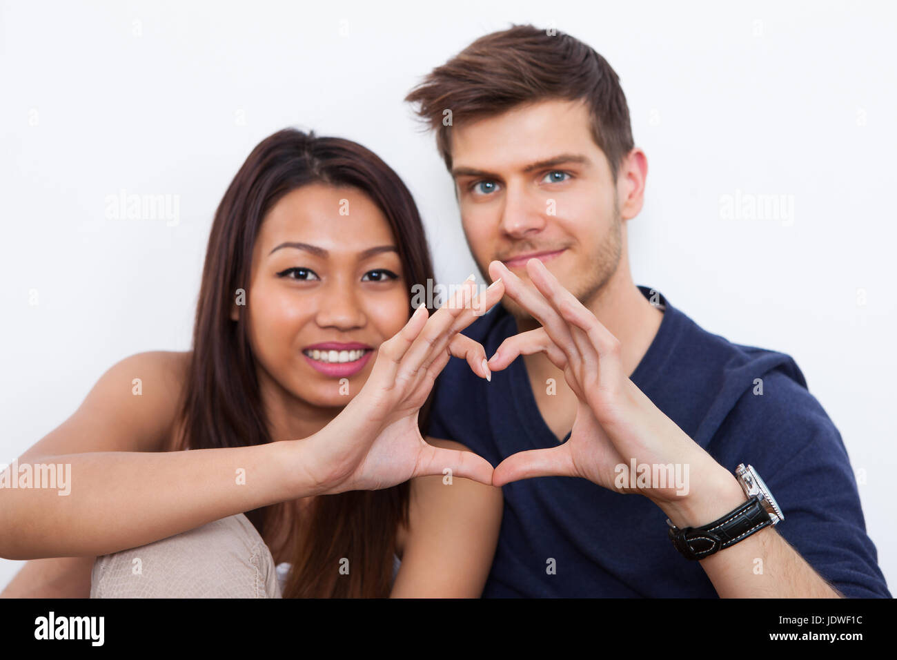 Portrait of young multiethnic couple making heart shape with hands at ...