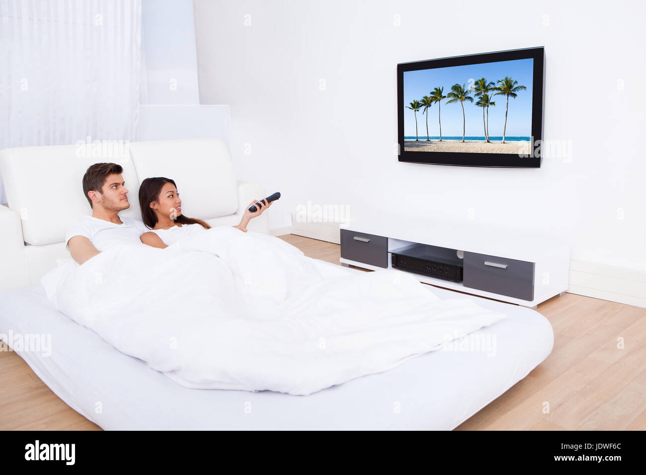 Young couple watching TV while lying in bed at home Stock Photo - Alamy