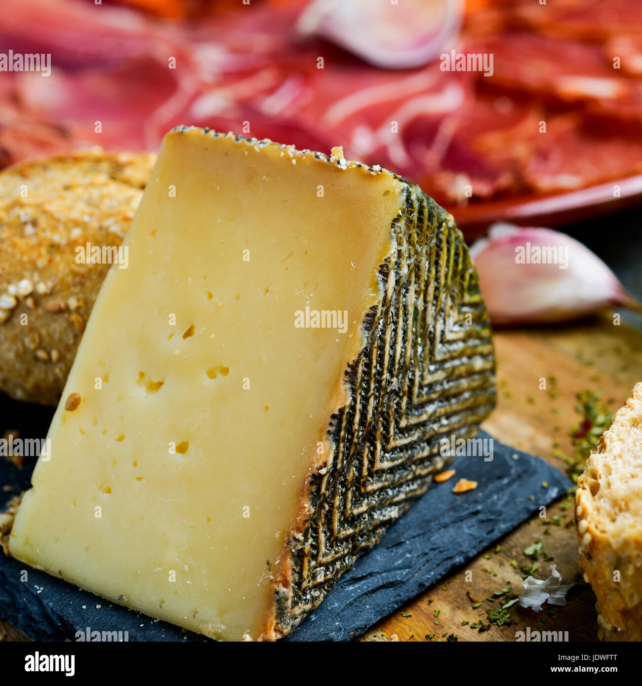 closeup of a piece of manchego cheese, and a plate with an assortment of different spanish cold meats as chorizo, cured pork tenderloin and serrano ha Stock Photo