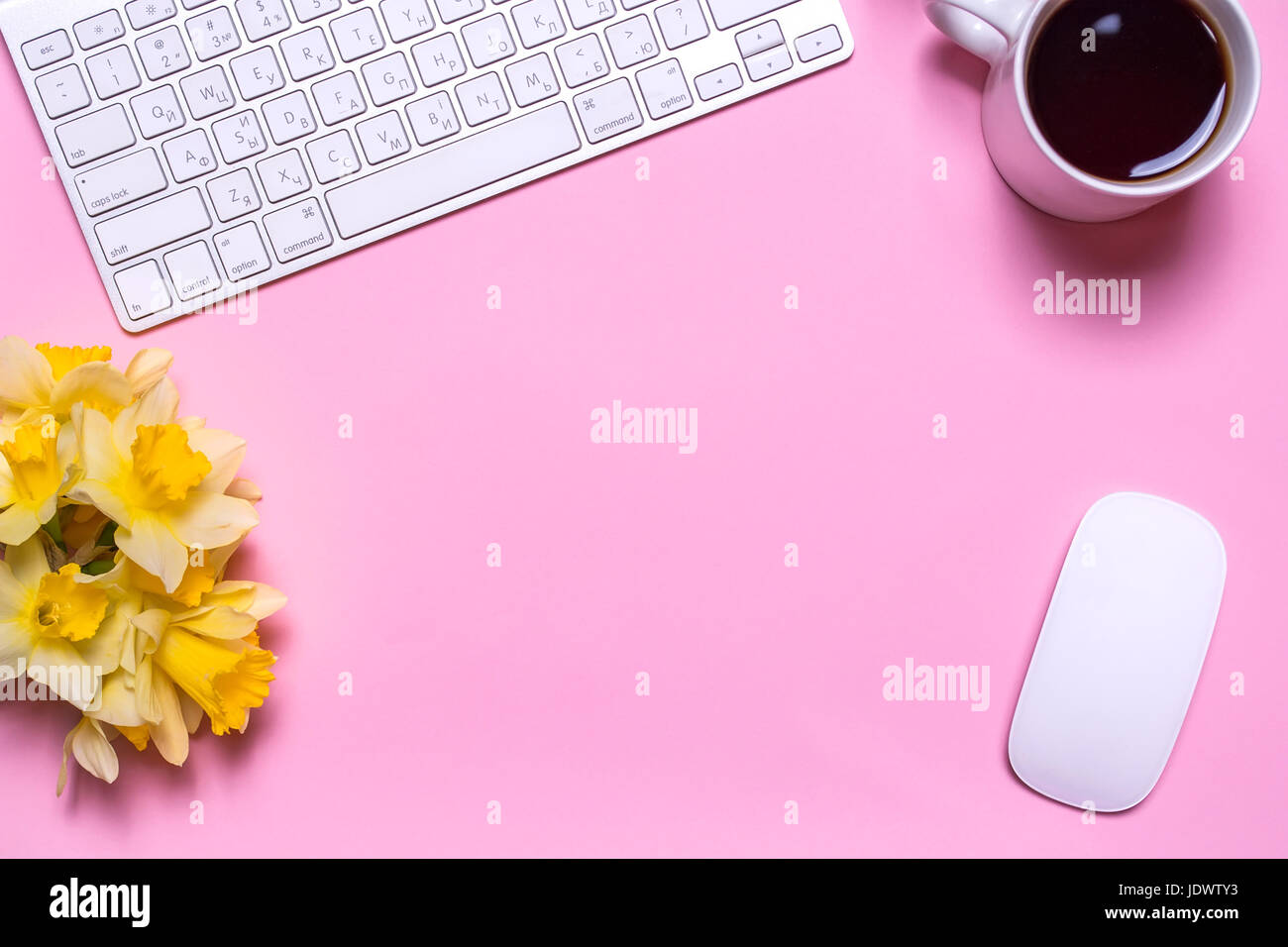 Office workplace with keyboard, a bouquet of daffodils, a cup of tea and a computer mouse on a pink background. Flat lay design, top view. Stock Photo