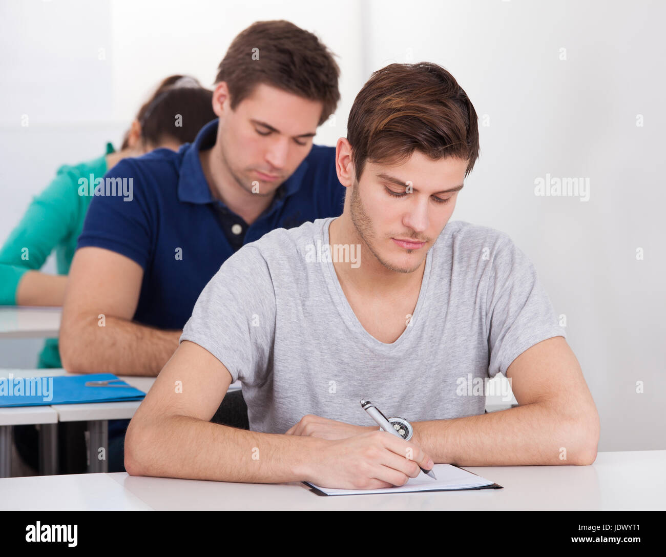 Portrait of male college student sitting at desk with classmates in ...