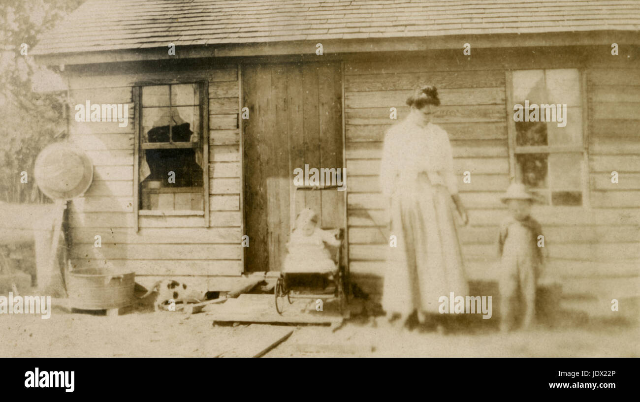 Antique c1905 photograph, mother, toddler, baby and a cat in front of small farmhouse. Location unknown, possibly Minnesota. SOURCE: ORIGINAL PHOTOGRAPH. Stock Photo