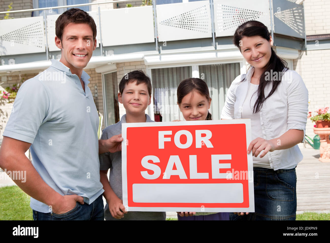 Portrait of young family selling their home holding for sale sign ...