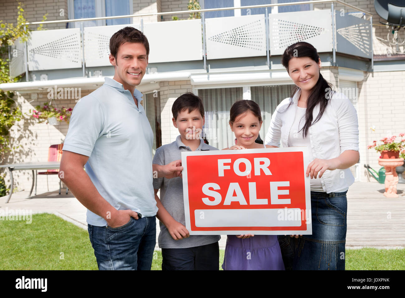 Portrait of family holding for sale sign standing outside their house ...