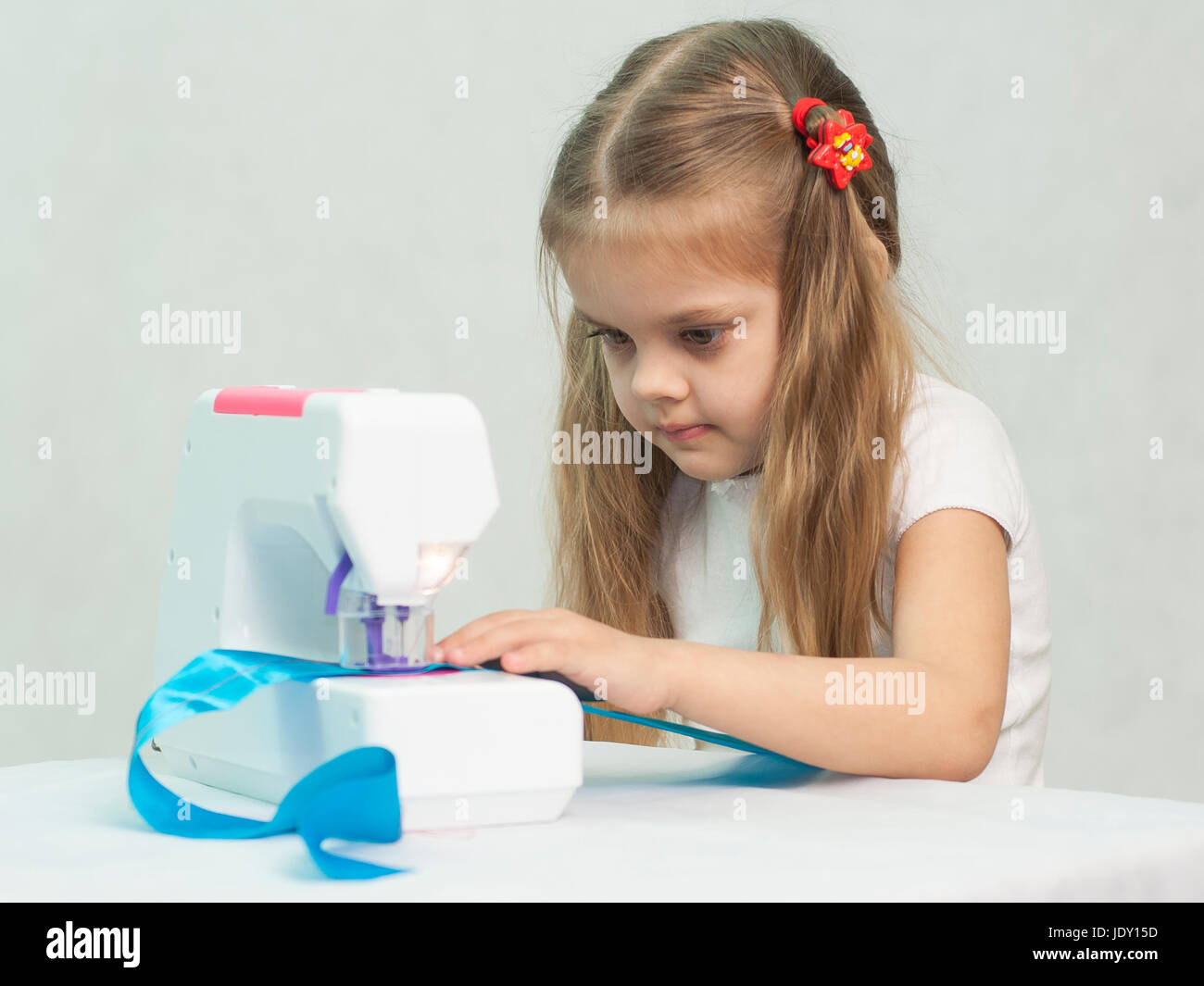 Girl sew on a children's sewing machine. Studio, a white background