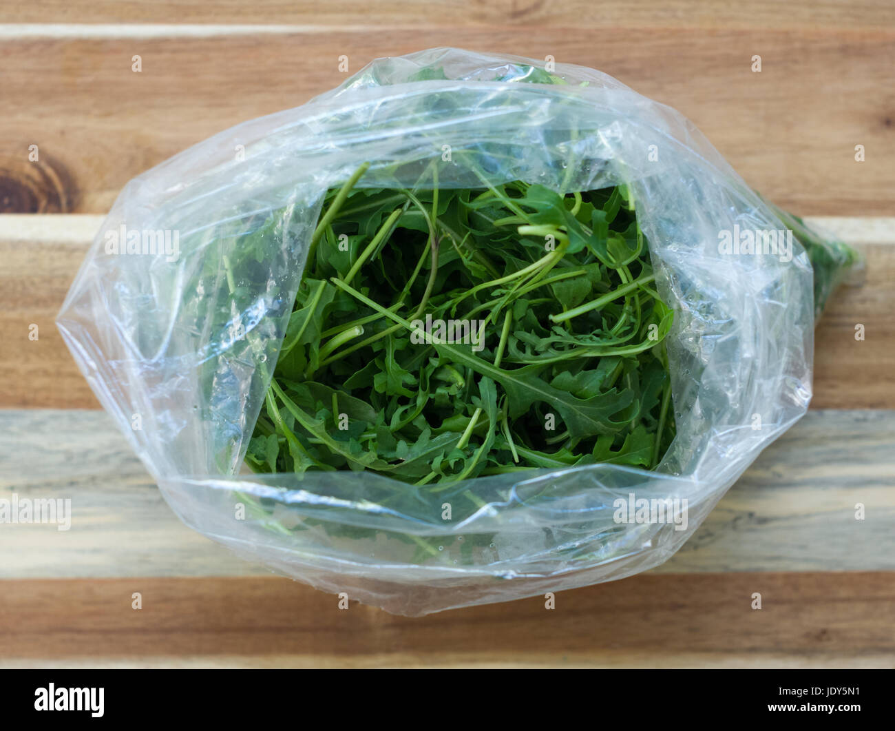 A large plastic bag filled with arugula (rocket) on a wooden chopping board Stock Photo