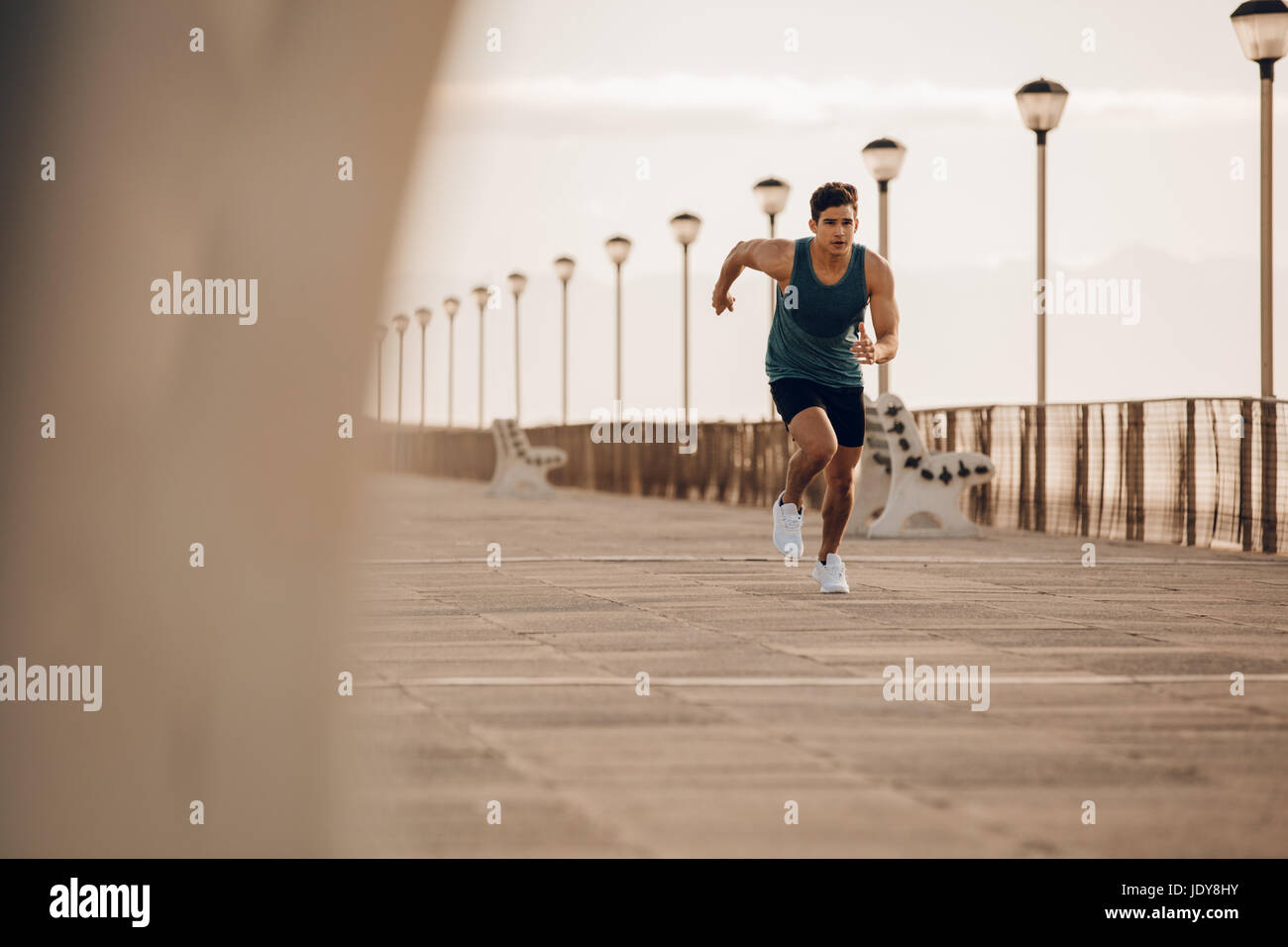 Full length shot of fit young man running fast on the promenade. Male runner sprinting in morning. Stock Photo