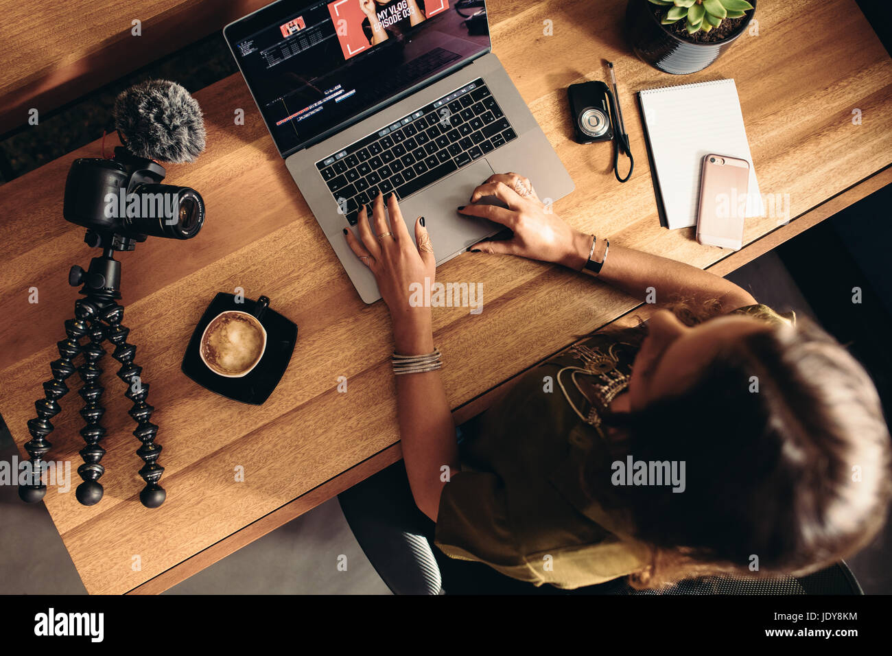 Top view of female vlogger editing video on laptop. Young woman working on computer with coffee and cameras on table. Stock Photo