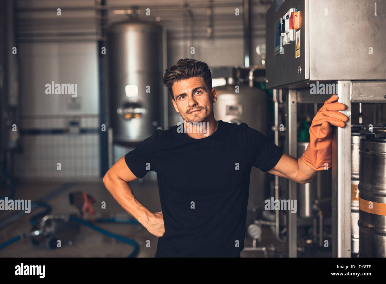 Male brewers working with industrial equipment at the brewery. Young man standing by beer filling machine at brewery factory. Stock Photo