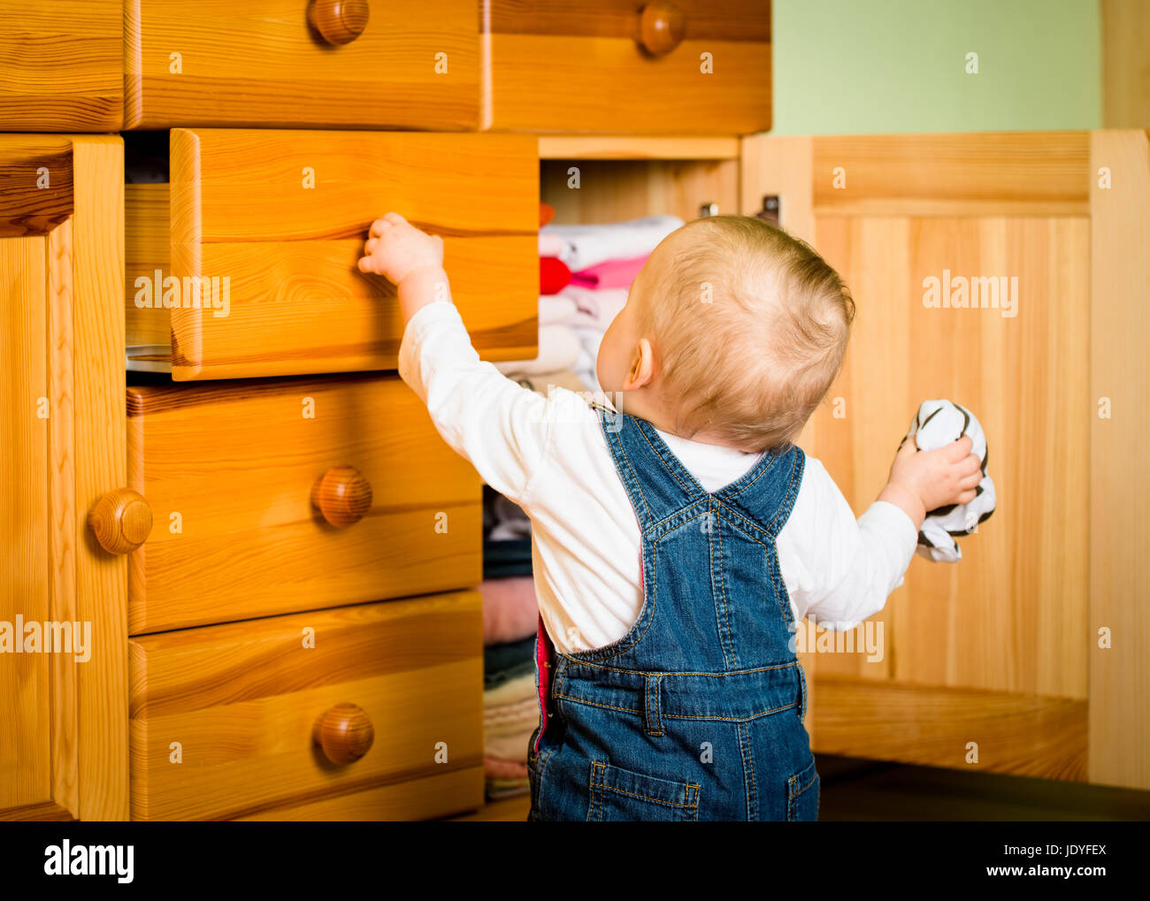 Baby opening drawer with clothes on wooden furniture home interior