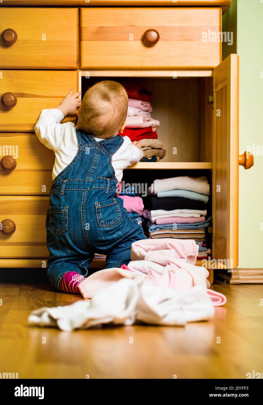 Baby throws out clothes from wooden furniture at home Stock Photo Alamy