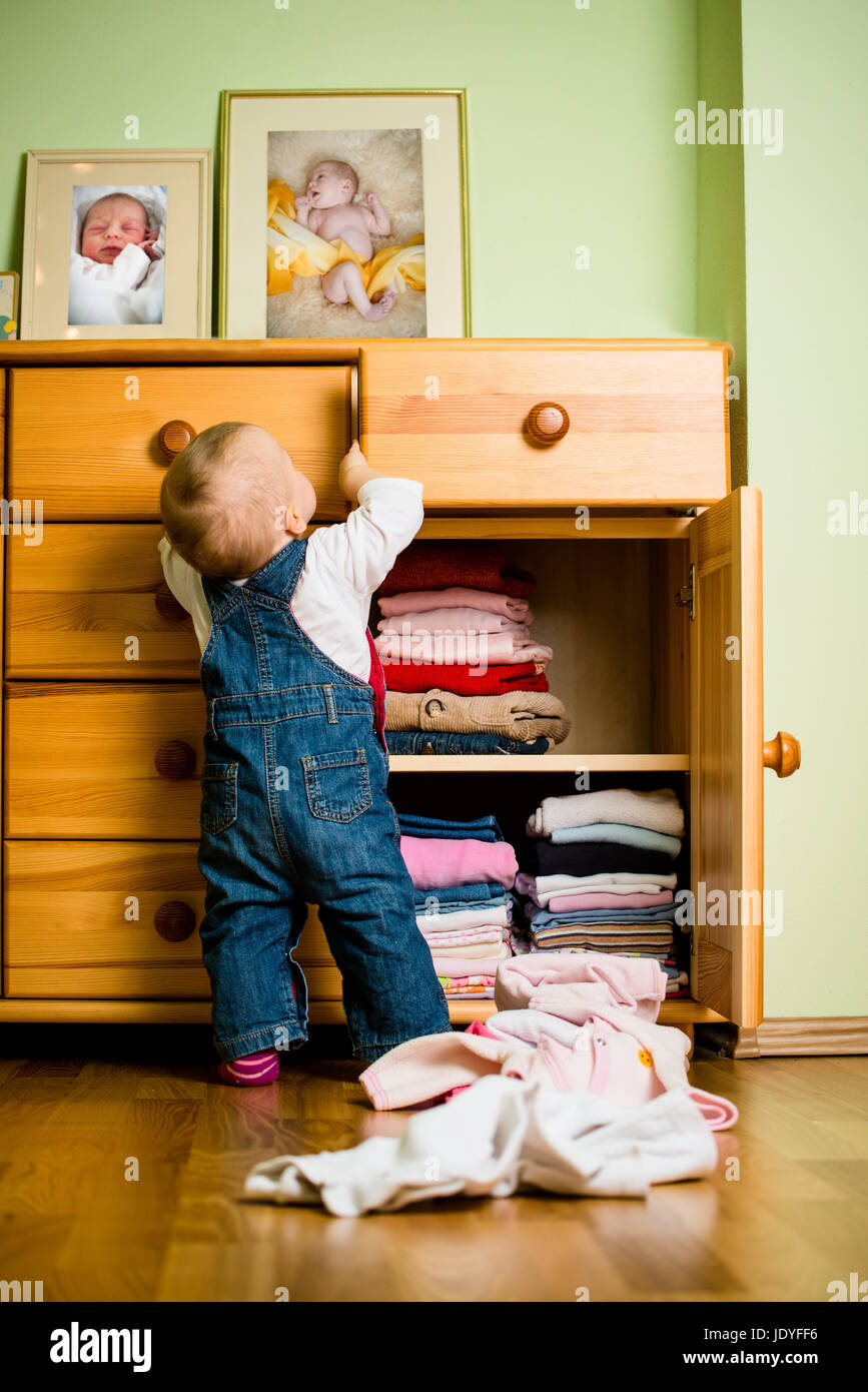 Baby throws out clothes from wooden furniture at home Stock Photo Alamy