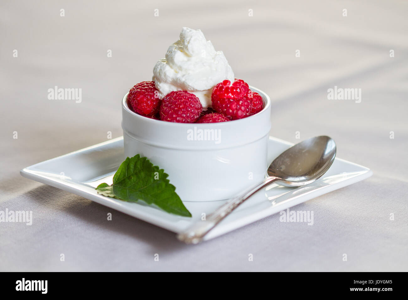 A dessert of Fresh Raspberries and whipped cream in restaurant setting. Stock Photo