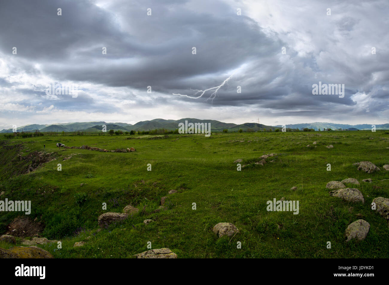 lightning storm clouds landscape in meadow summer day with mountain on horizon Stock Photo