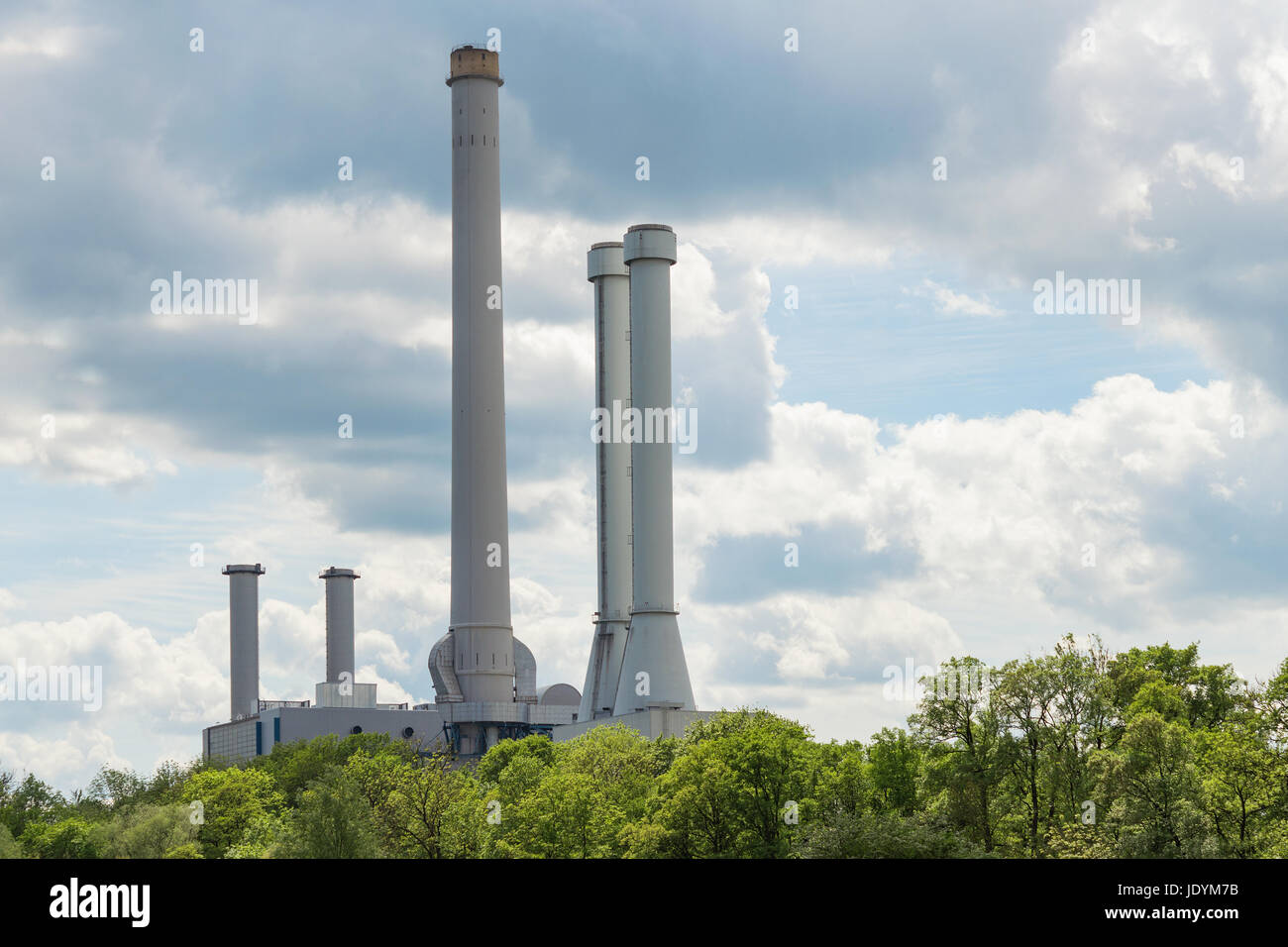 Industrial smokestack over green forest trees against clouds in sky Stock Photo