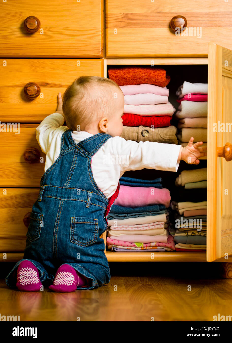 Baby throws out clothes from wooden furniture at home Stock Photo Alamy