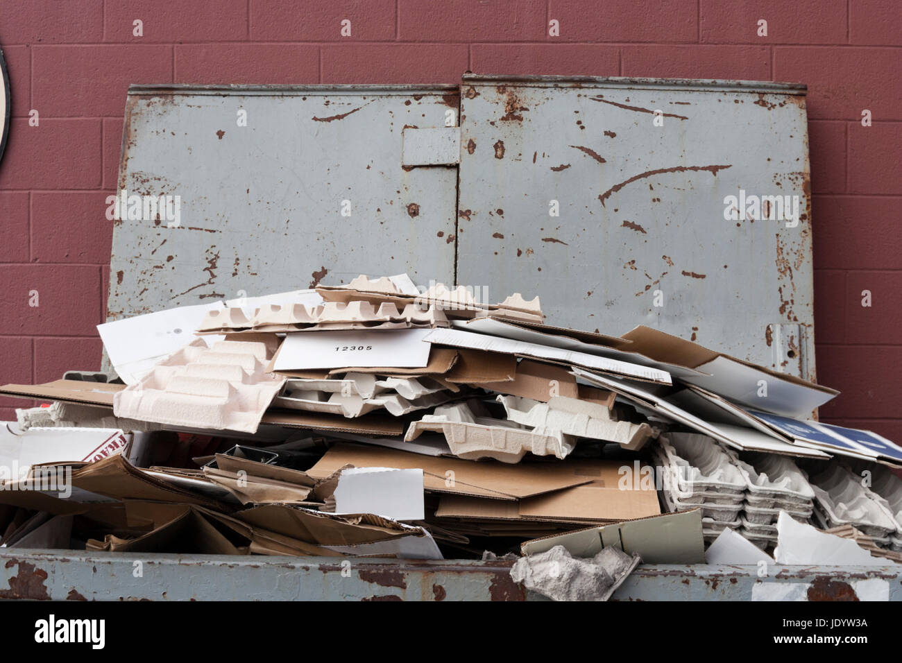 Close up of dumpster filled with cardboard for recycling. Lid open against reddish wall. Horizontal. Stock Photo