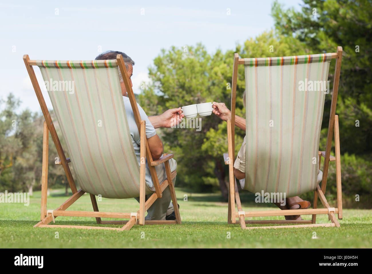 Couple sitting in deck chairs enjoying cups of coffee on the lawn Stock Photo