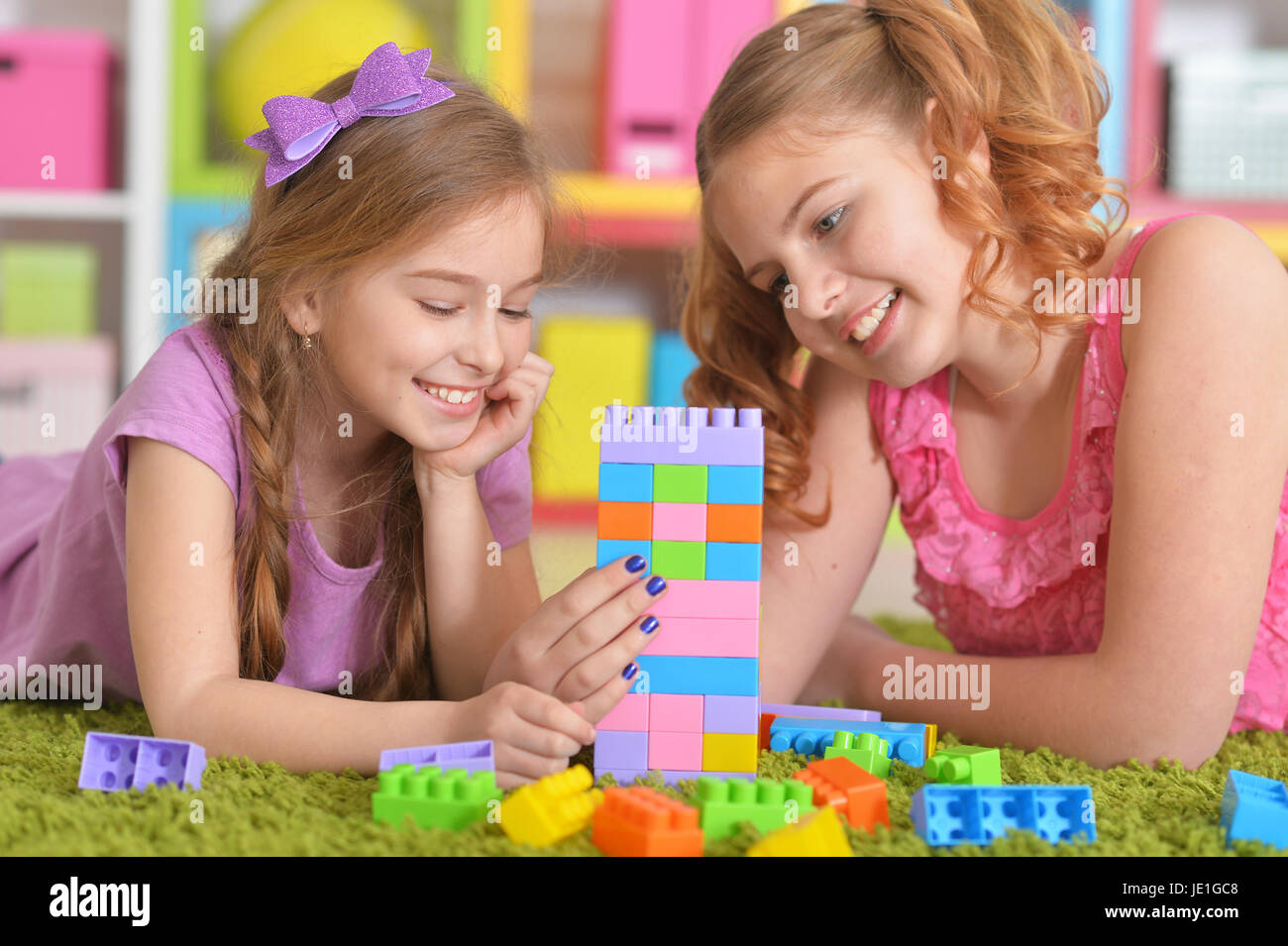 Cute girls playing with colorful plastic blocks in room Stock Photo - Alamy