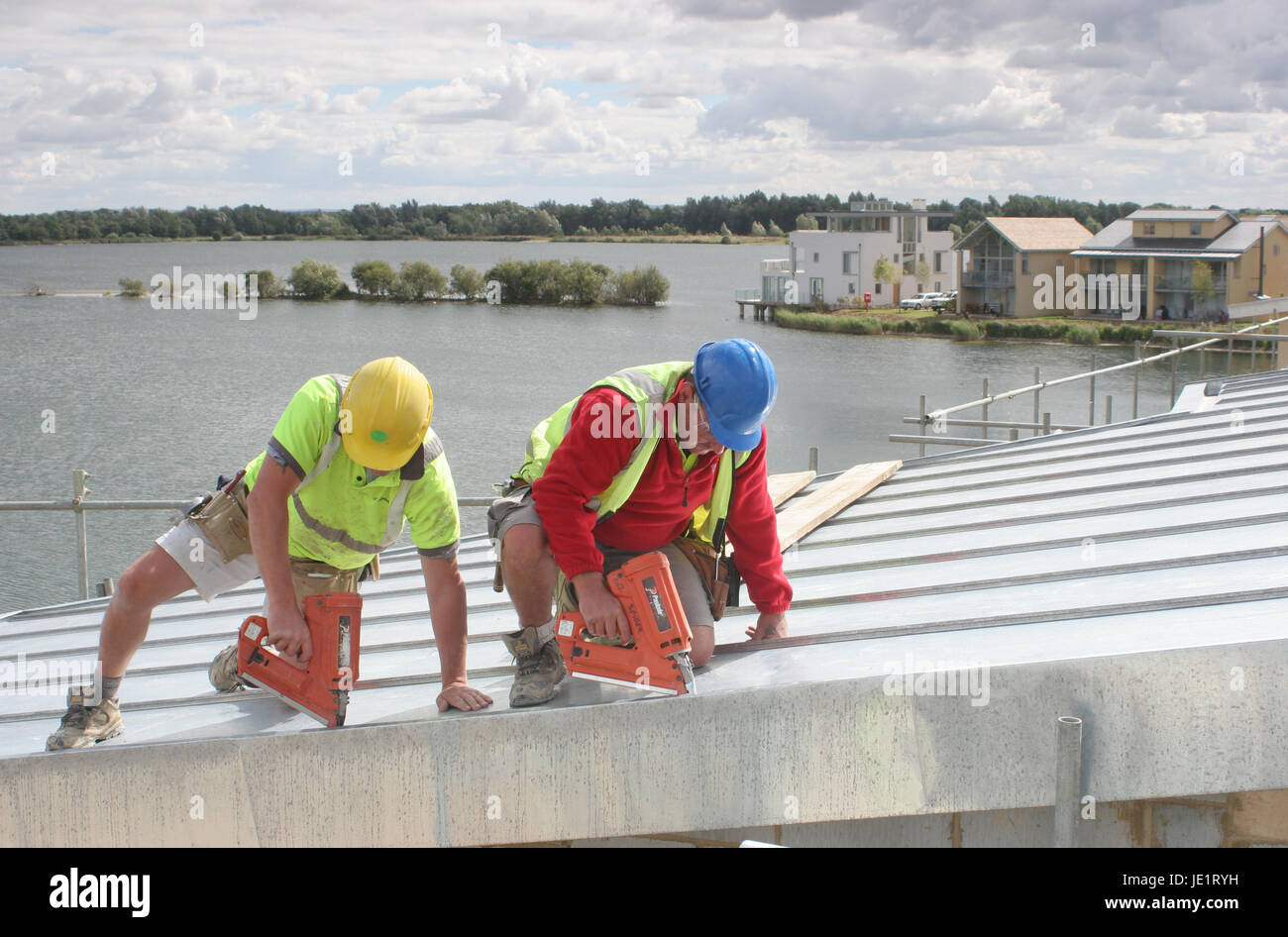 Two builders use gaspowered nail guns to fix zinc sheeting to the roof