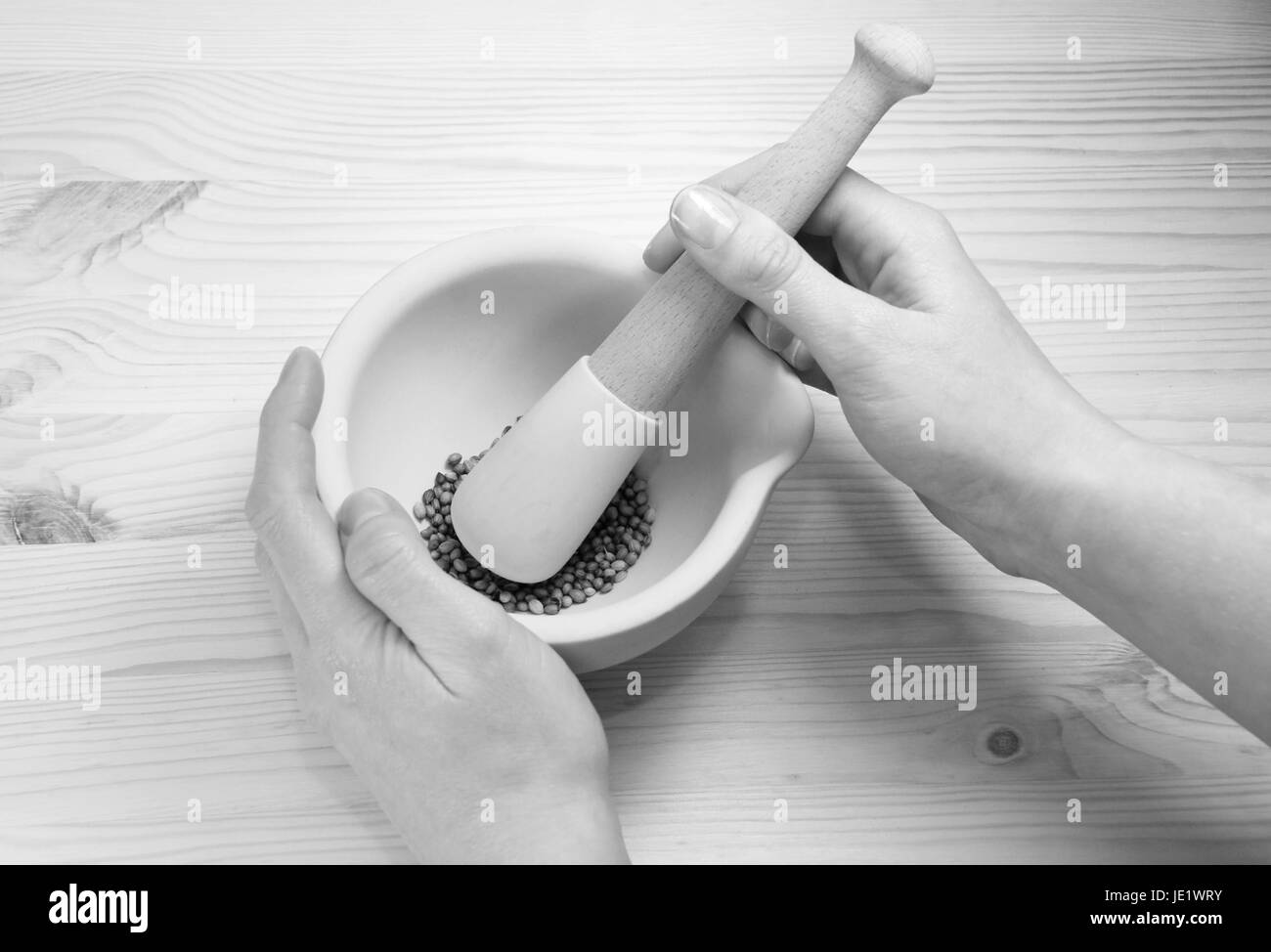A woman uses a pestle and mortar on a wooden table to crush whole