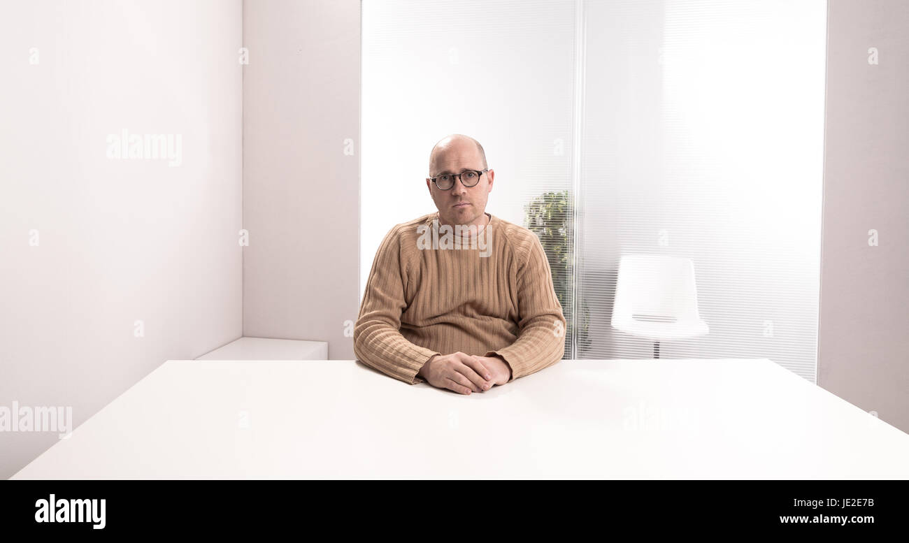 sad bald plump man with glasses in an empty office waiting for something that have to happen Stock Photo