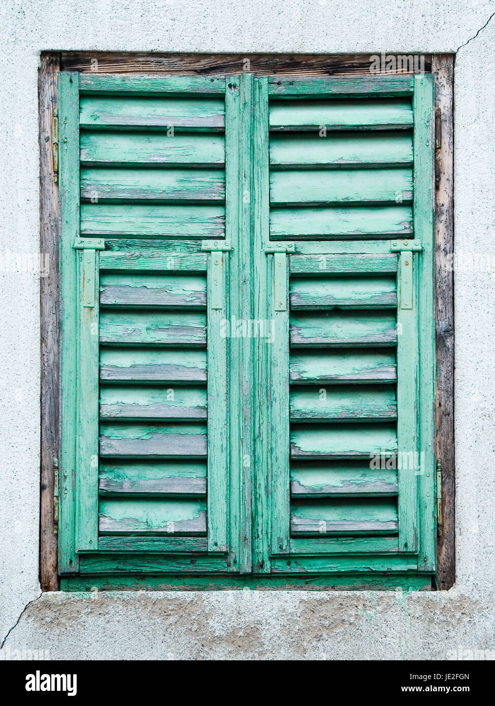 frontale Ansicht eines alten verwitterten Fensterladen mit grüner abblätternder Farbe in grauer Fassade Stock Photo