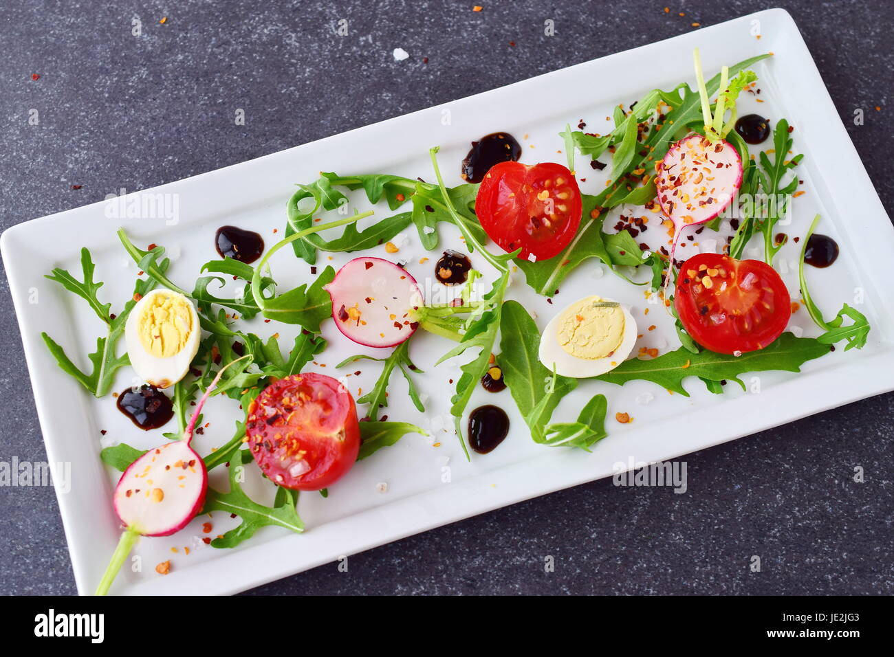 Fresh radish, cherry tomato, quail egg, ruccola with balsamic glaze on a white plate. Mediterranean lifestyle. Healthy food Stock Photo