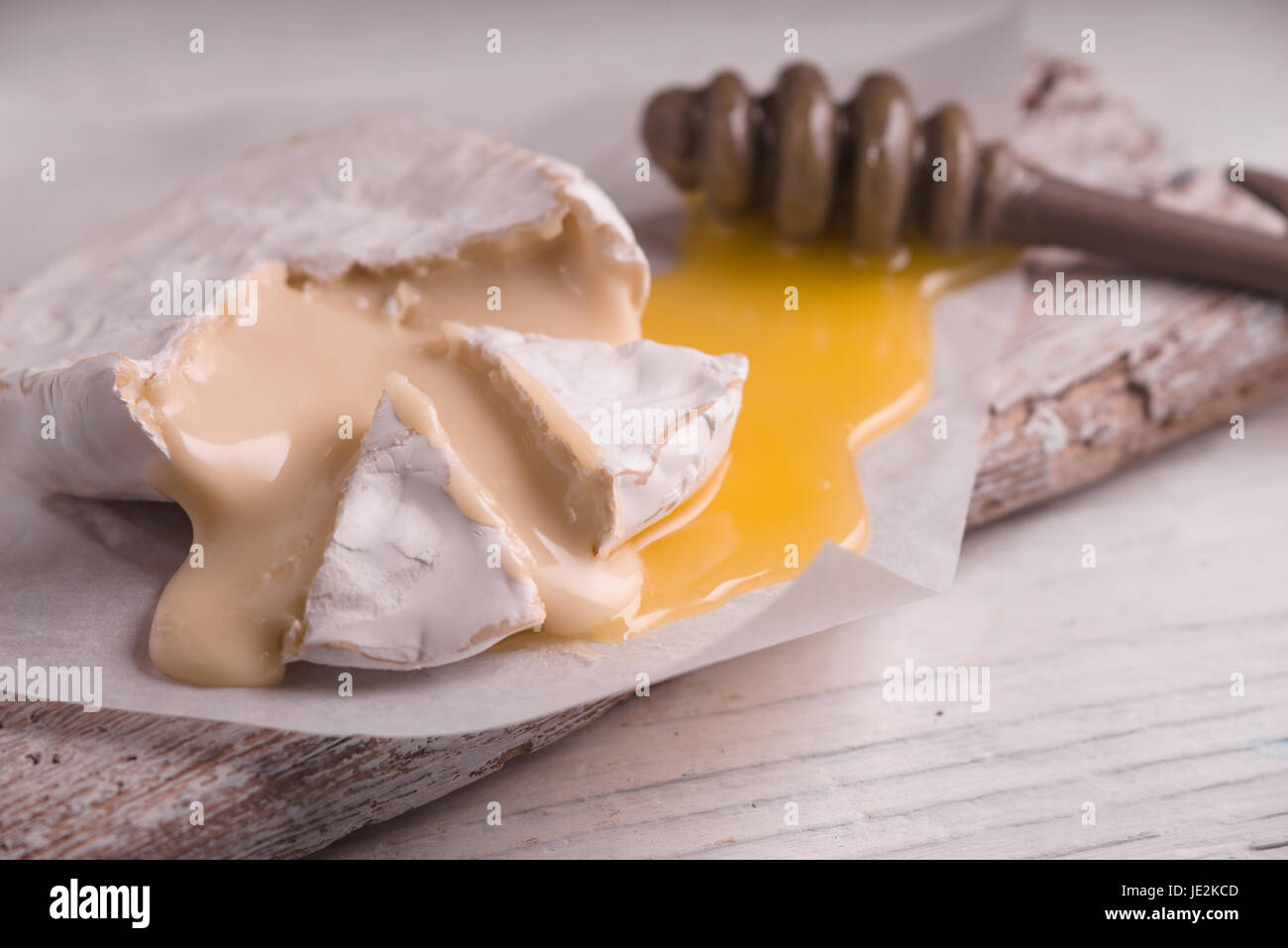 Brie cheese with honey on the parchment on the white wooden  table horizontal Stock Photo