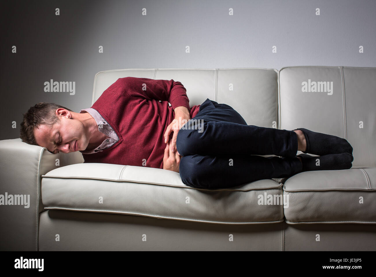 Young man suffering from severe belly pain, being overwhelmed by the debilitating condition of celiac disease/Crohn's disease/strong anxiety Stock Photo