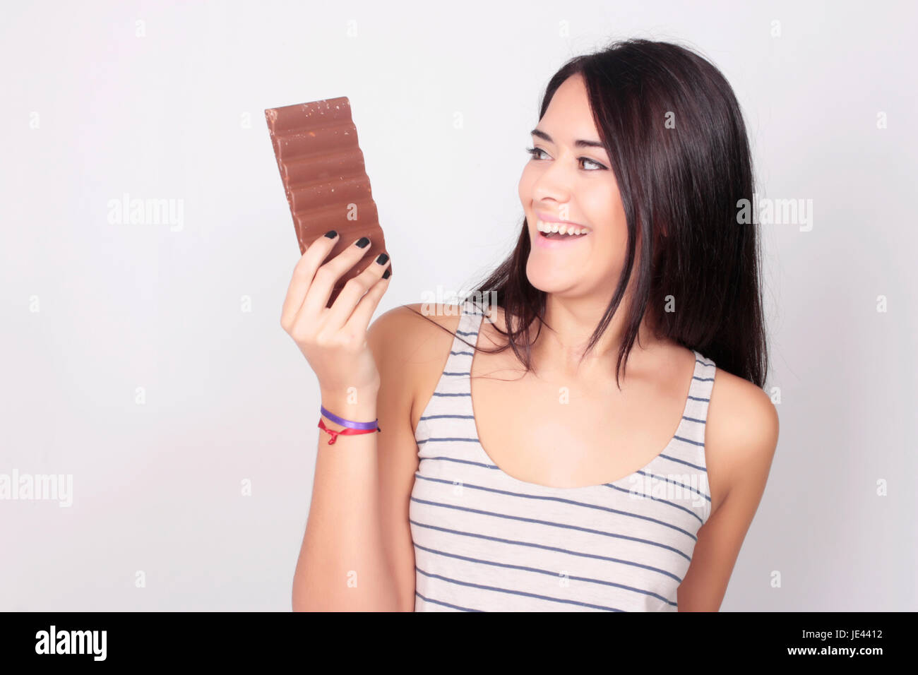 Young woman eating a chocolate bar. Beautiful caucasian girl enjoying chocolate with pleasure. Stock Photo