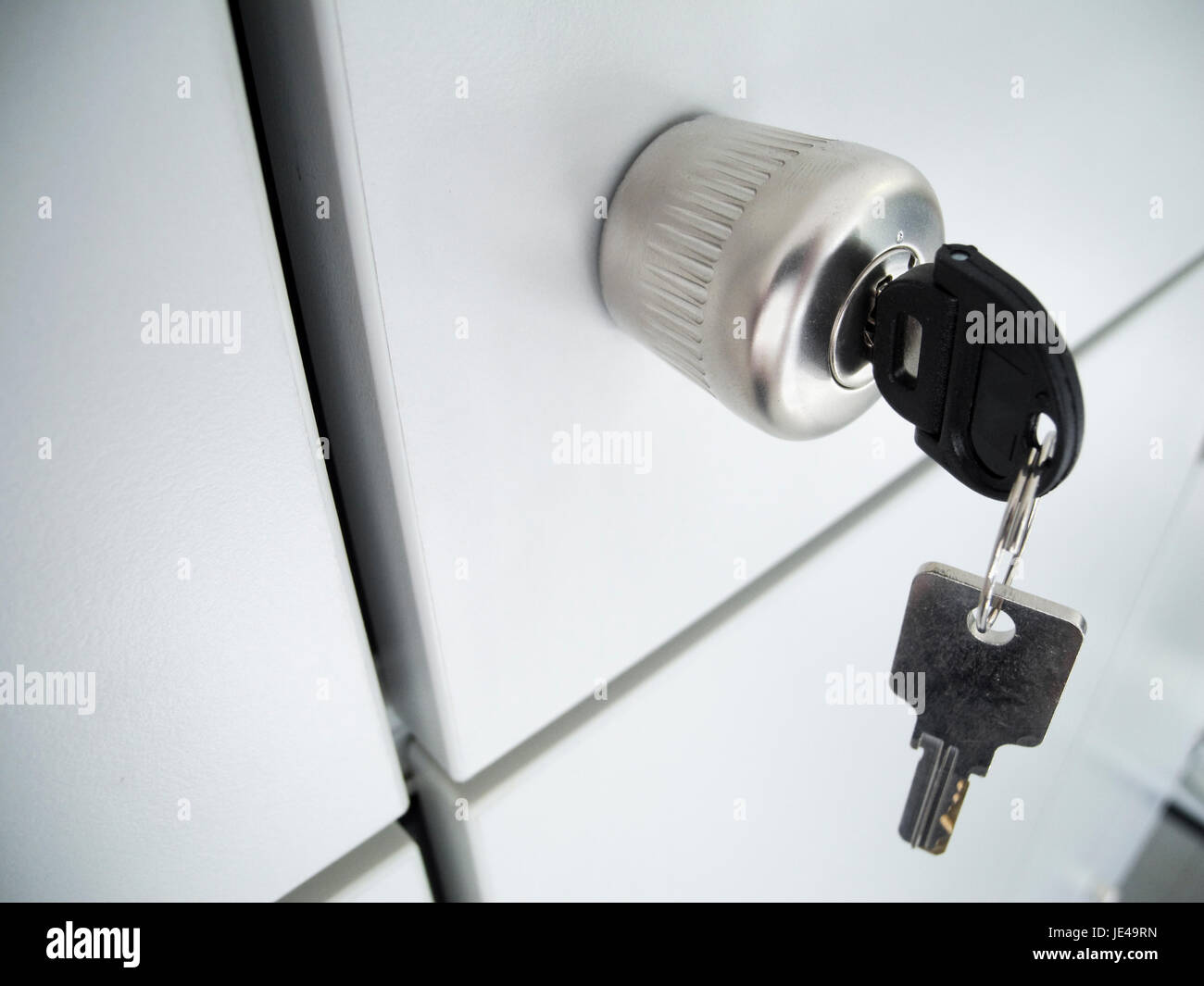 Detailaufnahme einer grauen Schranktür mit rundem Griff und steckenden und hängenden Schlüssel sowie sich kreuzende Abstandsspalten in Schrägansicht Stock Photo