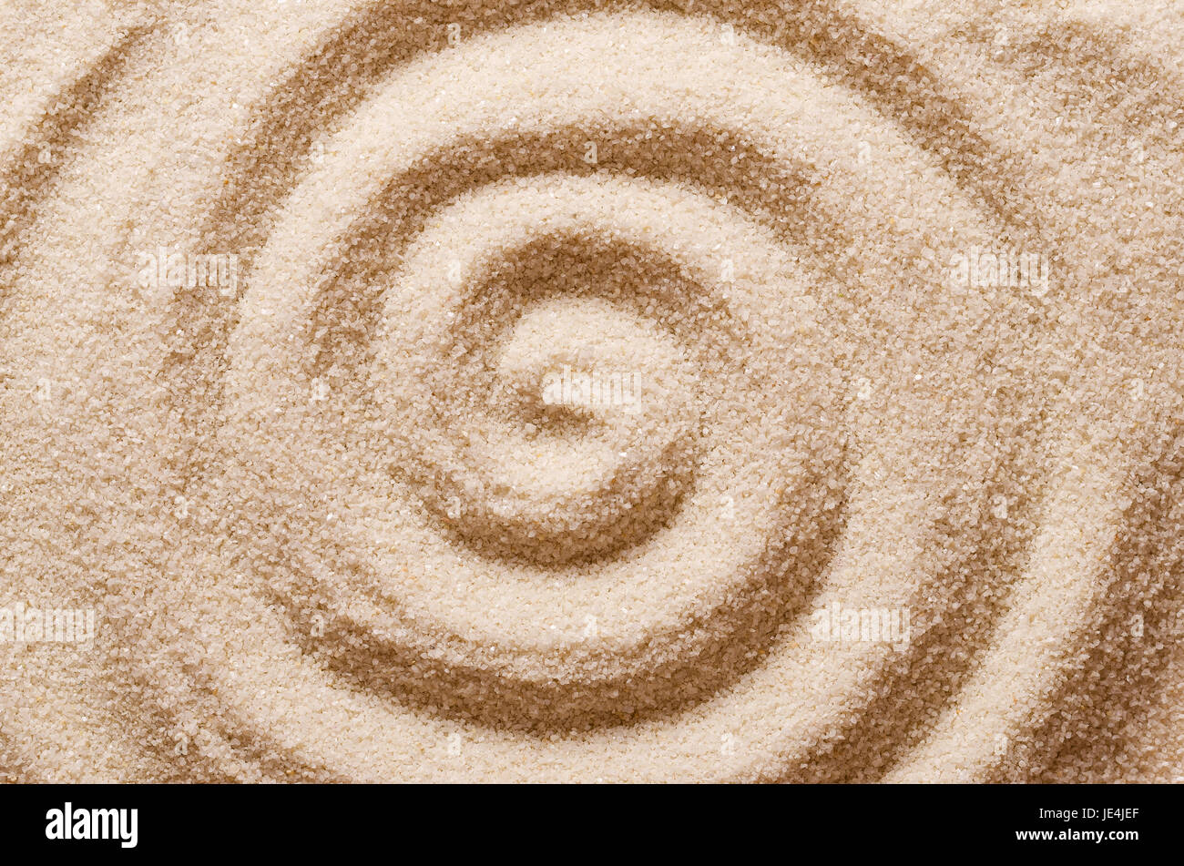 Spiral in the sand. Archimedean spiral made with the finger in dry ocherous sand. Macro photo close up from above. Stock Photo