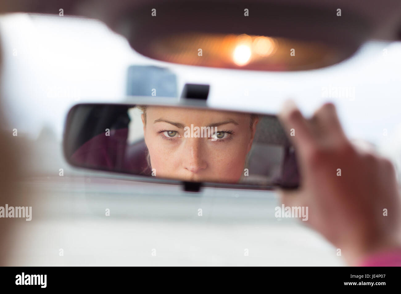 Beautiful young lady looking back through the rear view mirror from the