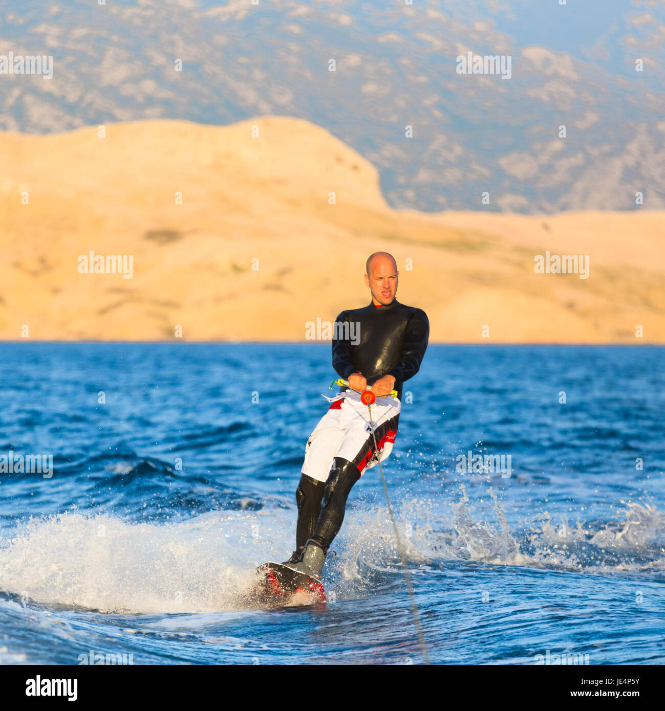 Wakeboarder in wetsuit riding in sunset. Wakeboarding is a surface water  sport which involves riding a wakeboard over the surface of a body of water  Stock Photo - Alamy